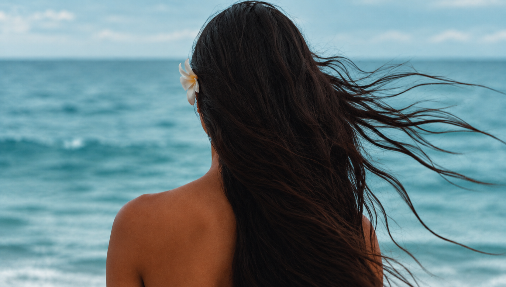 A woman with a frangipani flower in her hair looking out over the ocean
